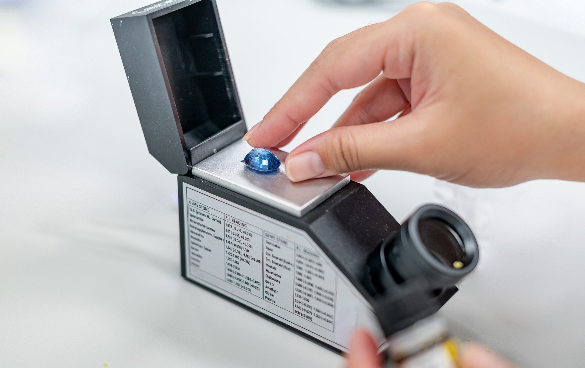 Female hand holding the blue precious stone and put on the refractometer for confirm the type of stone